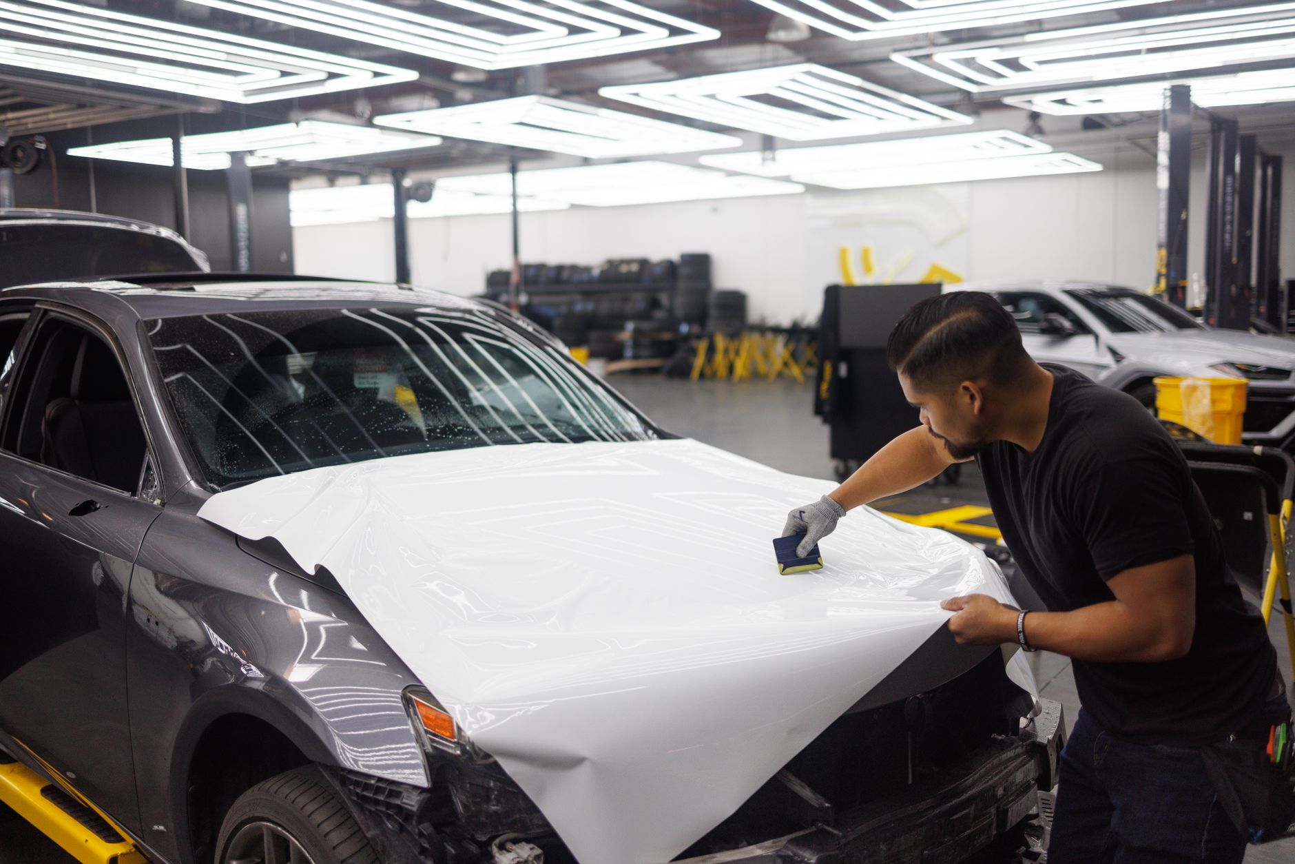 Technician applying a protective film to a car hood with a squeegee