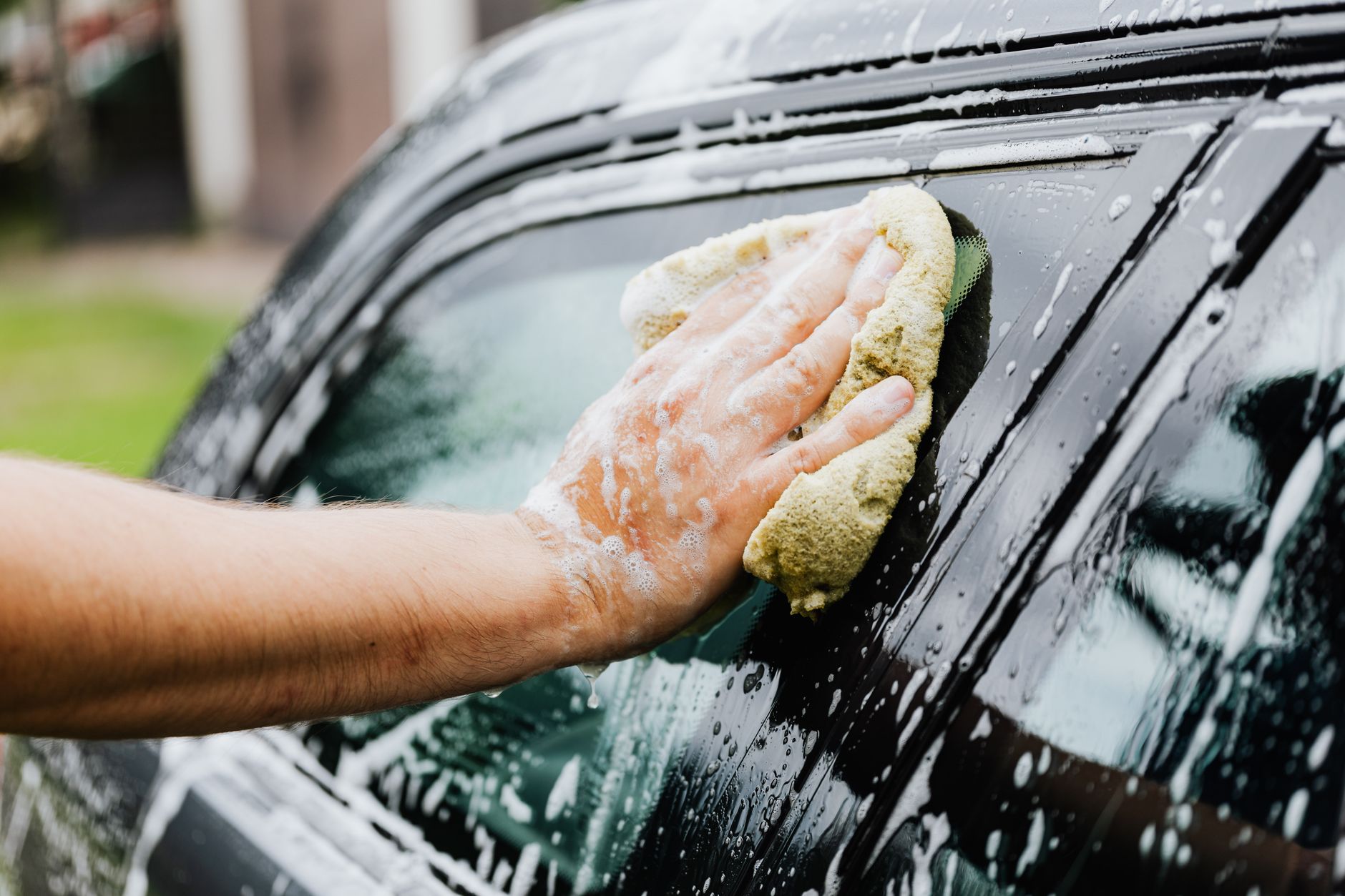 Hand scrubbing a car with a soapy sponge