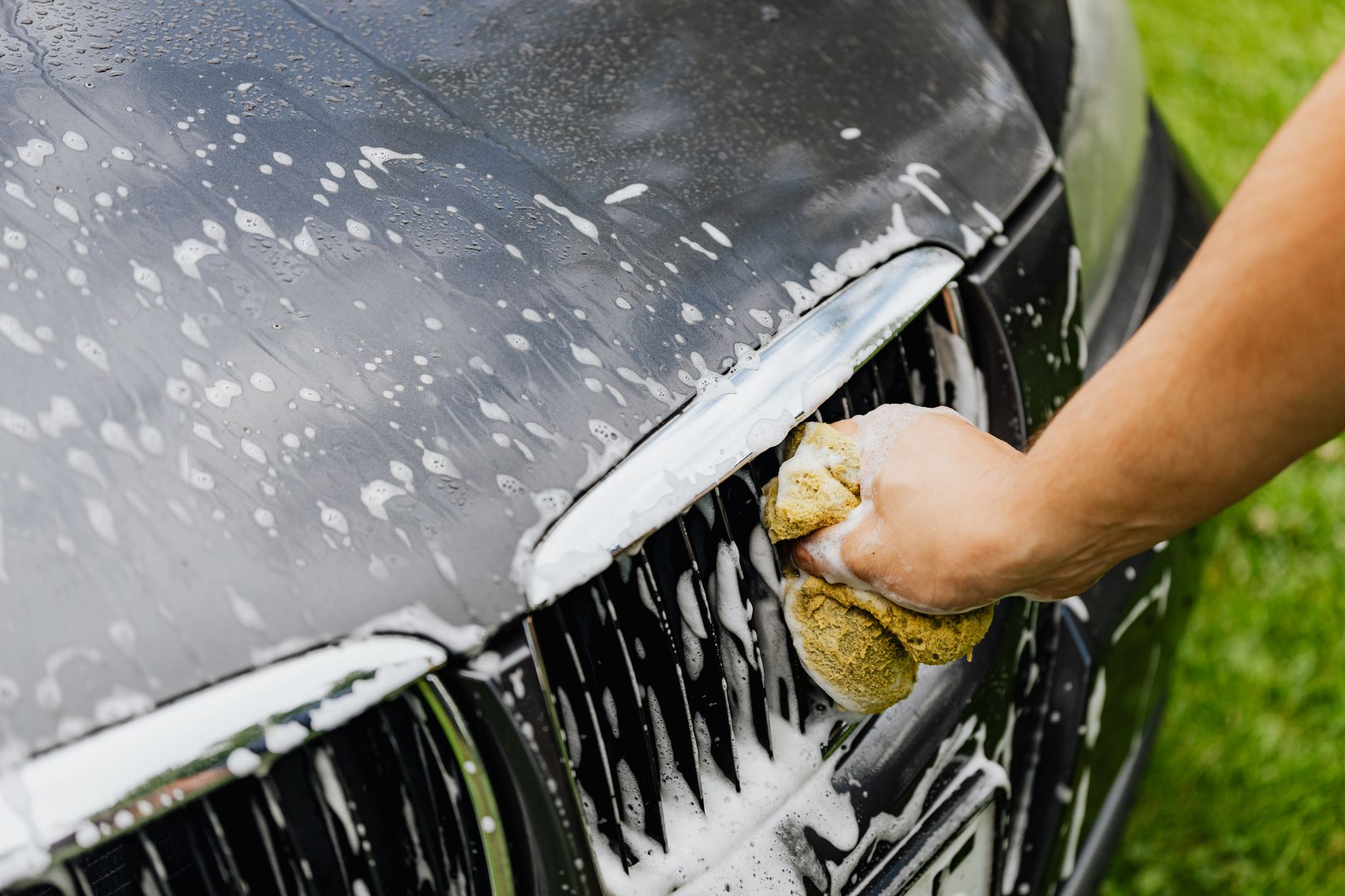 Hand washing a car grille with a soapy sponge during a pre-coating wash