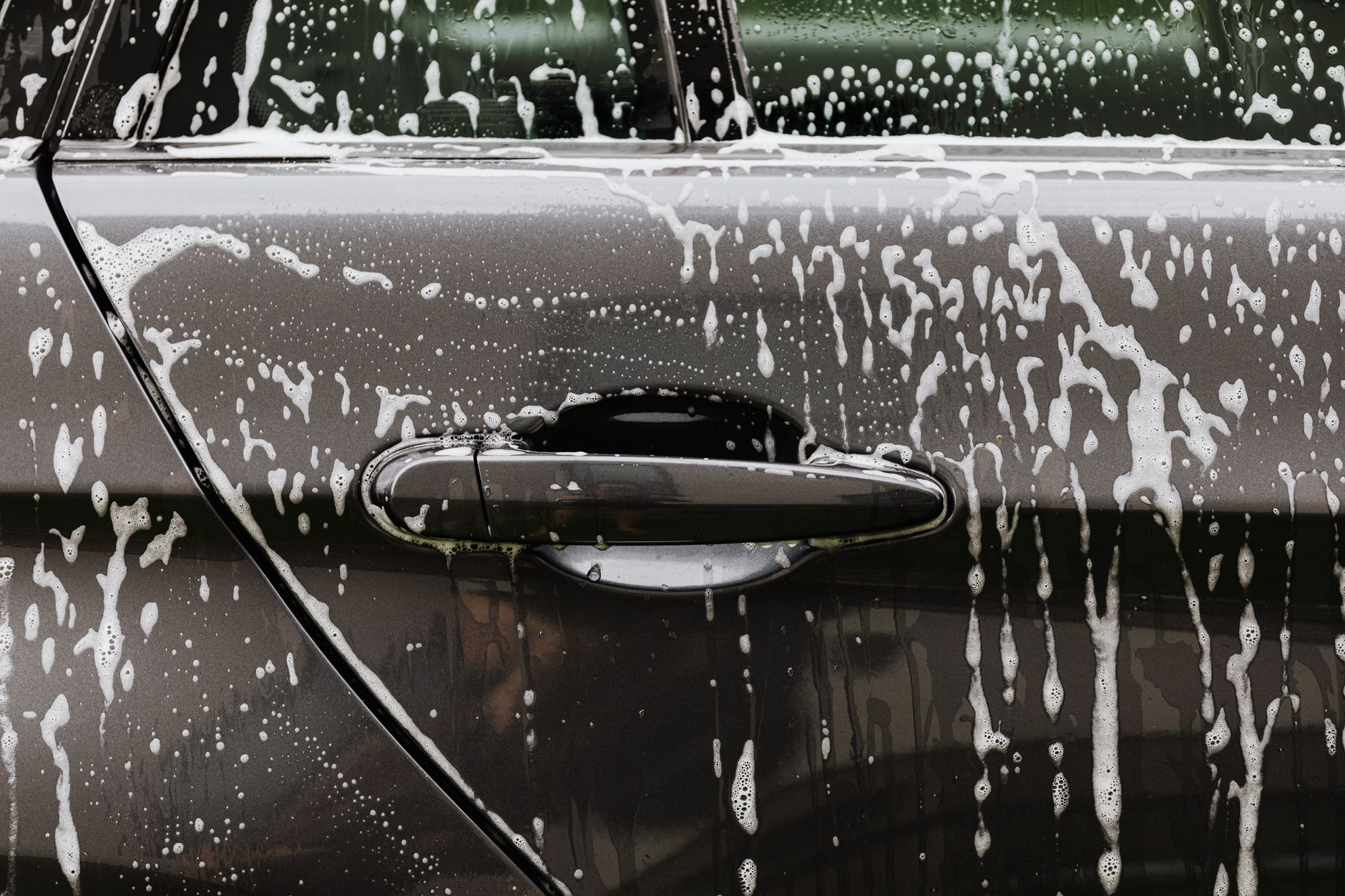 Close-up of soap suds on a black car door during a wash