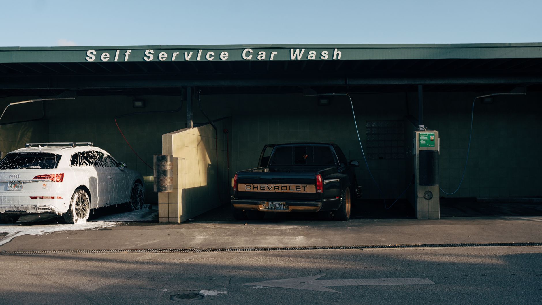 A self-service car wash bay with a foam-covered car and a pickup truck side by side