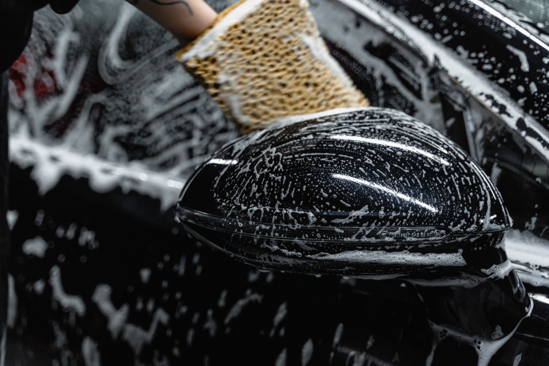 Hand scrubbing a car mirror with a soapy sponge at a car wash