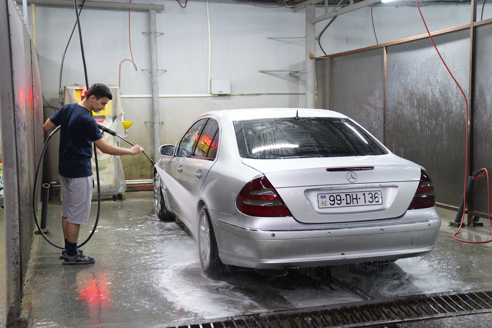 A man using a hose to wash a silver car inside an indoor self-service car wash bay